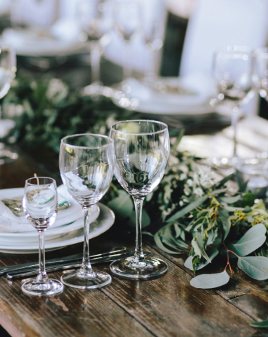 Close-up of elegant table setting with assorted glassware, greenery and white plates arranged for a wedding reception