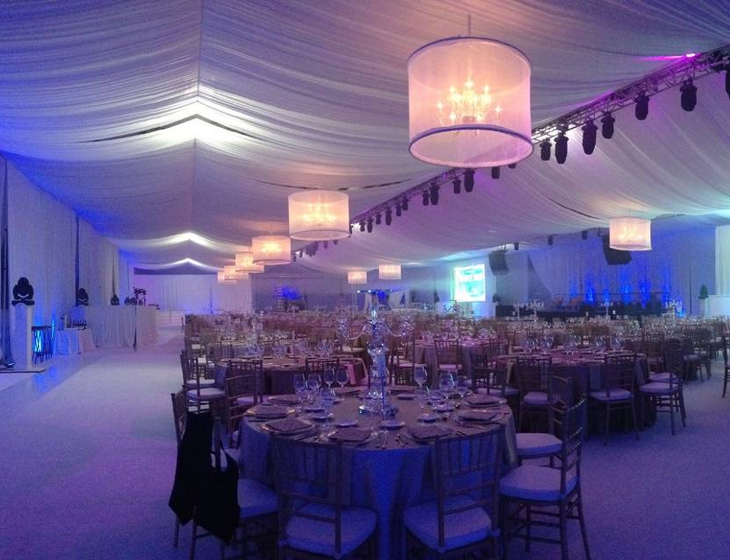 Elegant reception at Sun ‘n Fun with draped white ceiling, chandeliers, blue uplighting, and round tables with gold chairs