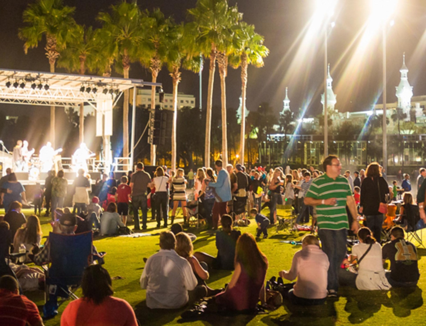 Night concert at Curtis Hixon Waterfront Park with stage lights, palm trees, and a large crowd enjoying outdoor music