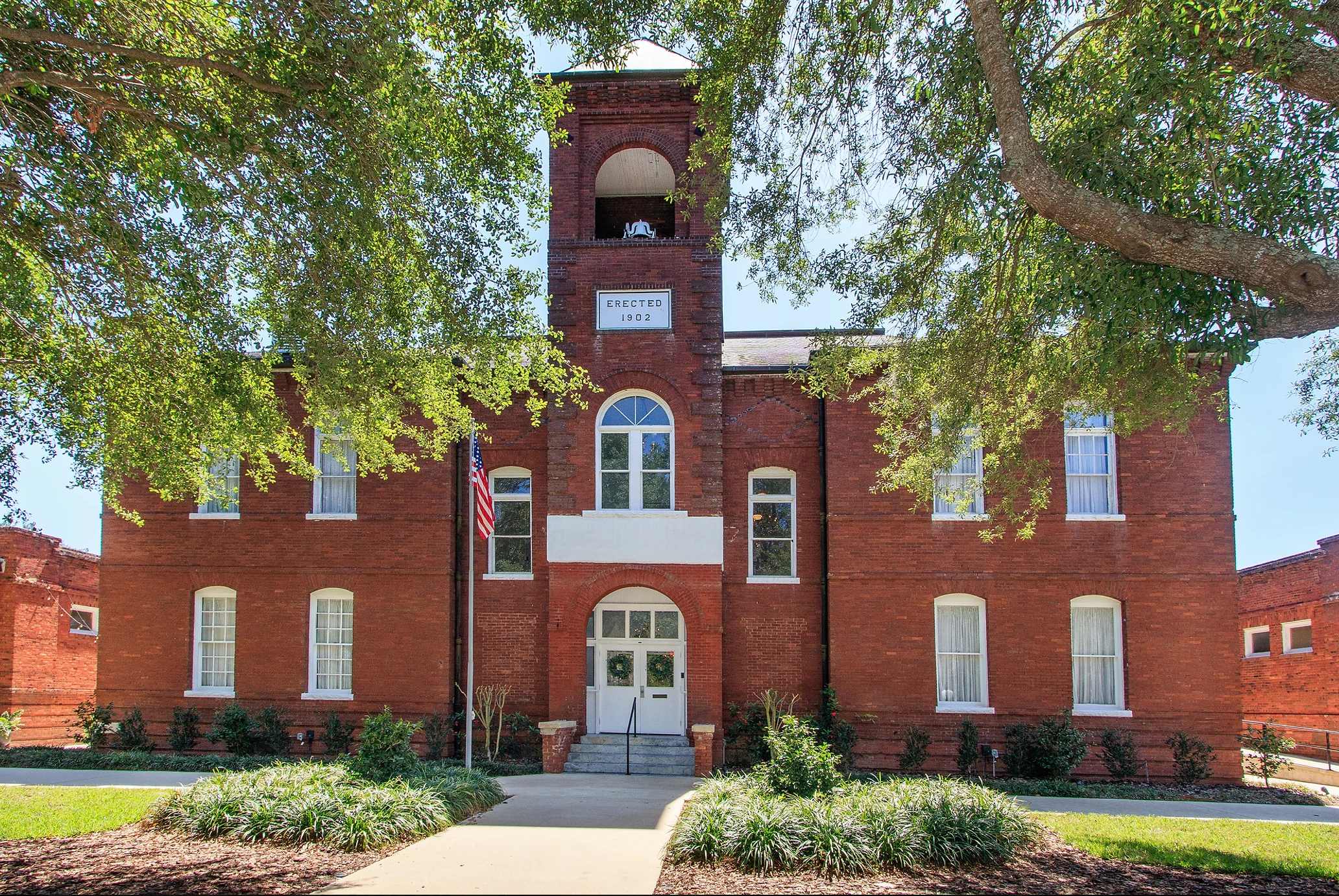 Exterior view of Historic Venue 1902 featuring red brick architecture, arched windows, and lush green trees