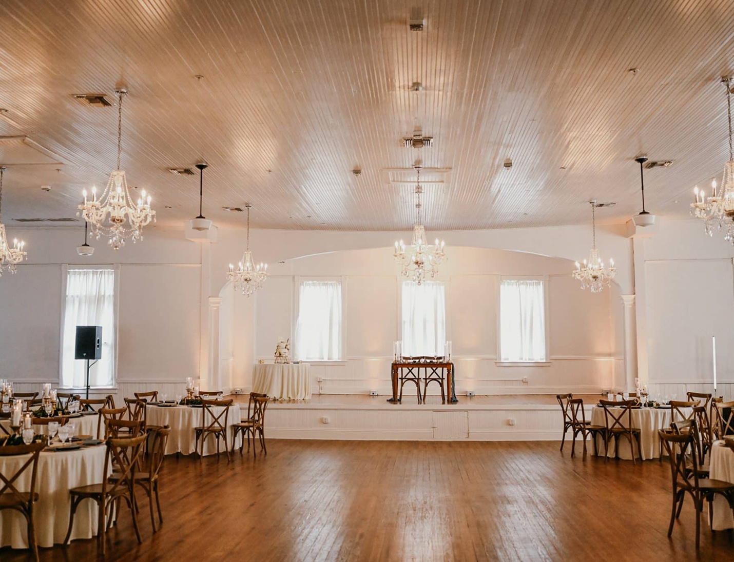 Elegant reception setup at Historic Venue 1902 with wooden floors, crystal chandeliers, round tables, and soft decor