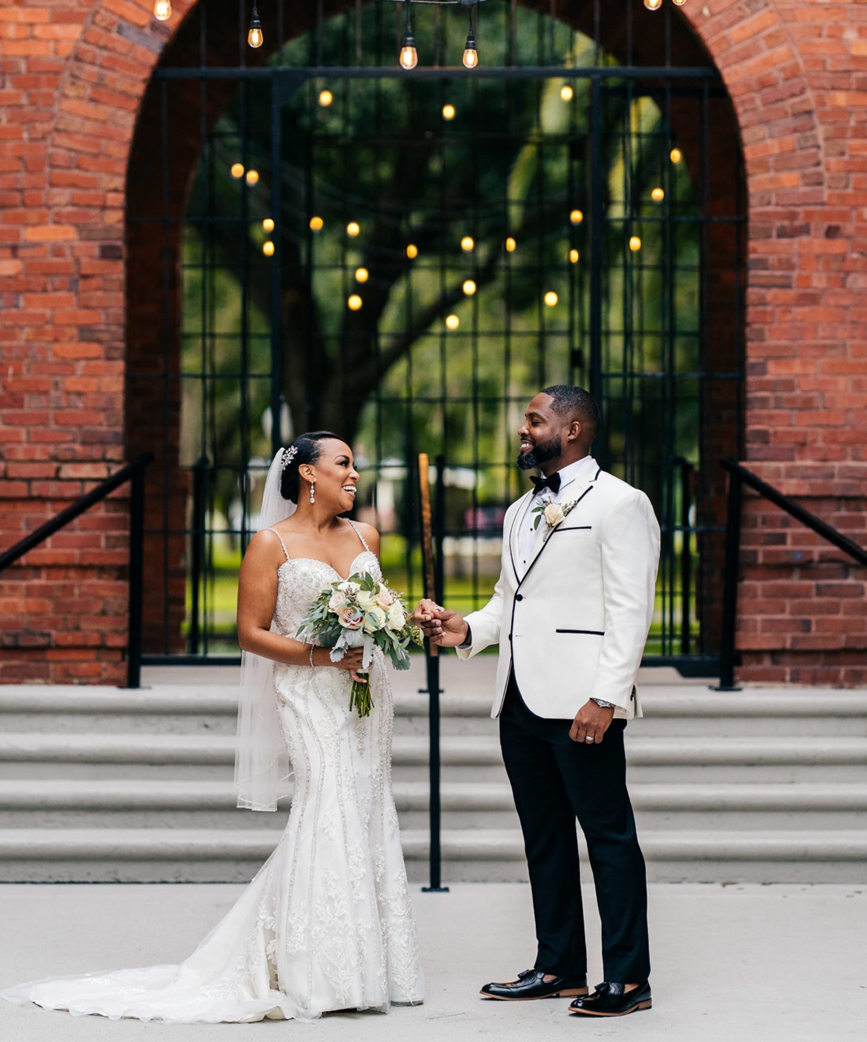 Bride and groom sharing a joyful moment in front of a brick archway and string lights at Historic Venue 1902