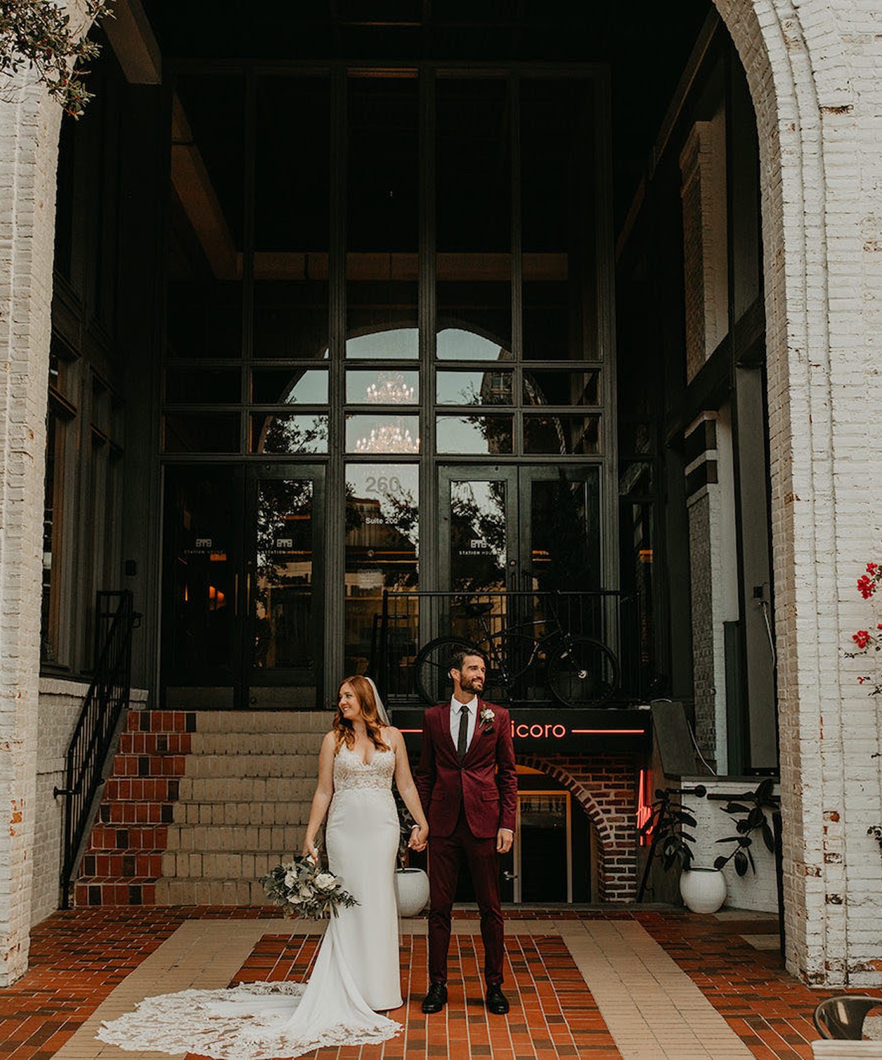 Bride and groom standing outside Station House, framed by brick archways and tall glass windows