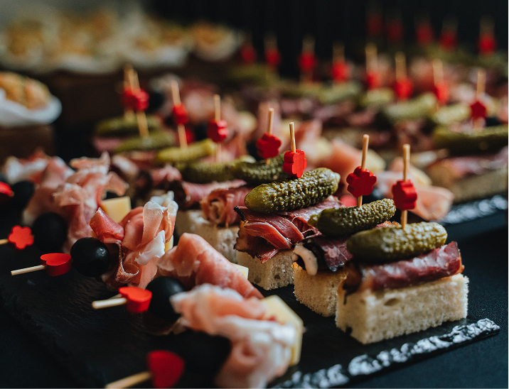 Elegant bite-sized appetizers with prosciutto, olives, and pickles served on bread squares for a catered even