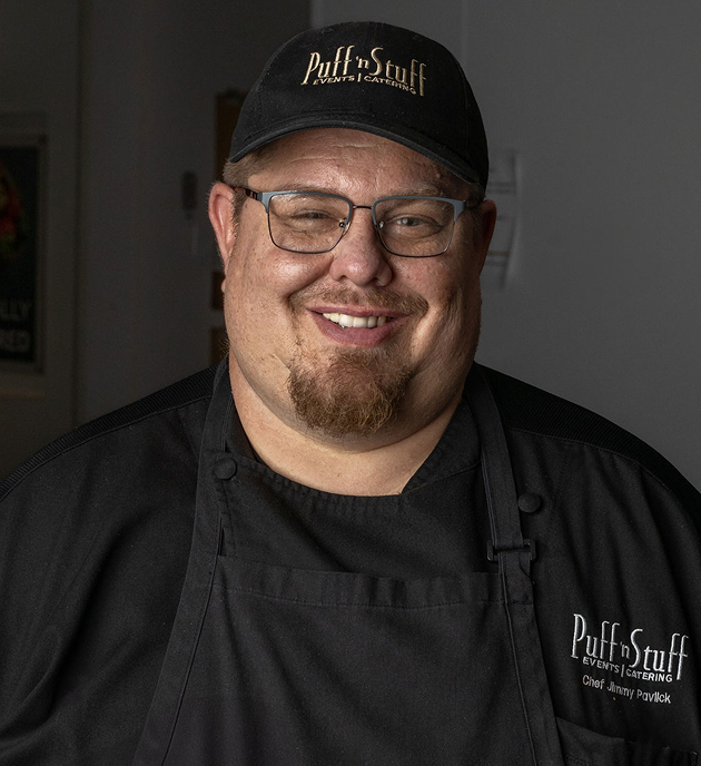 Member of the Puff ’n Stuff Catering team smiling while wearing a branded uniform and hat