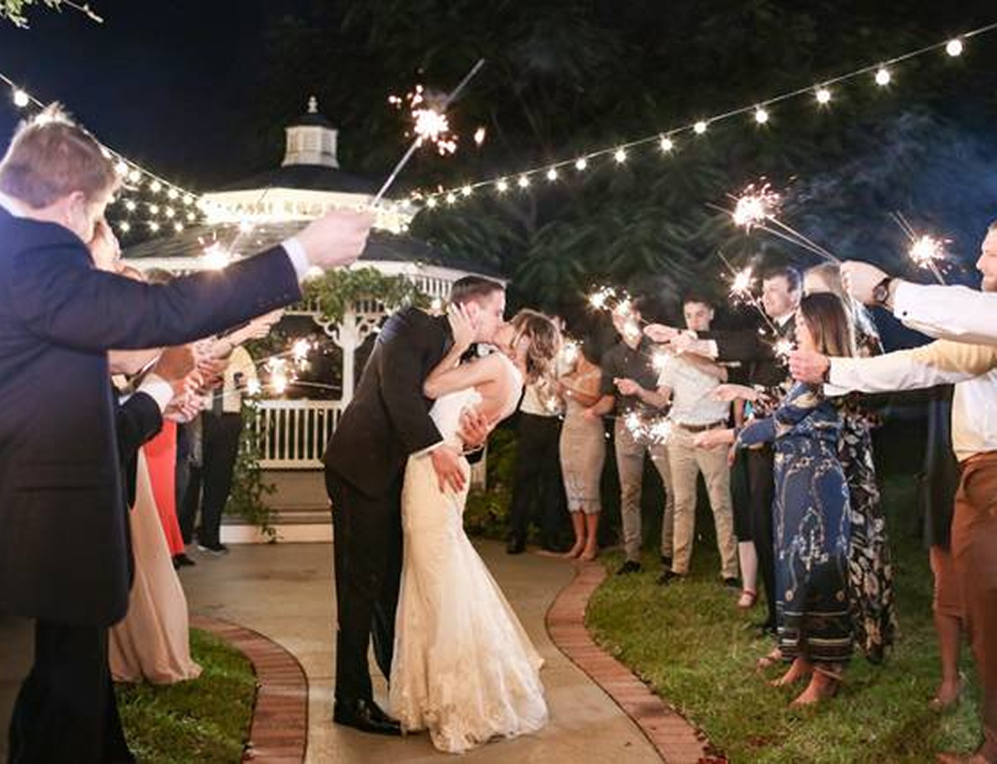 Bride and groom kissing under string lights at Davis Islands Garden Club surrounded by guests holding sparklers