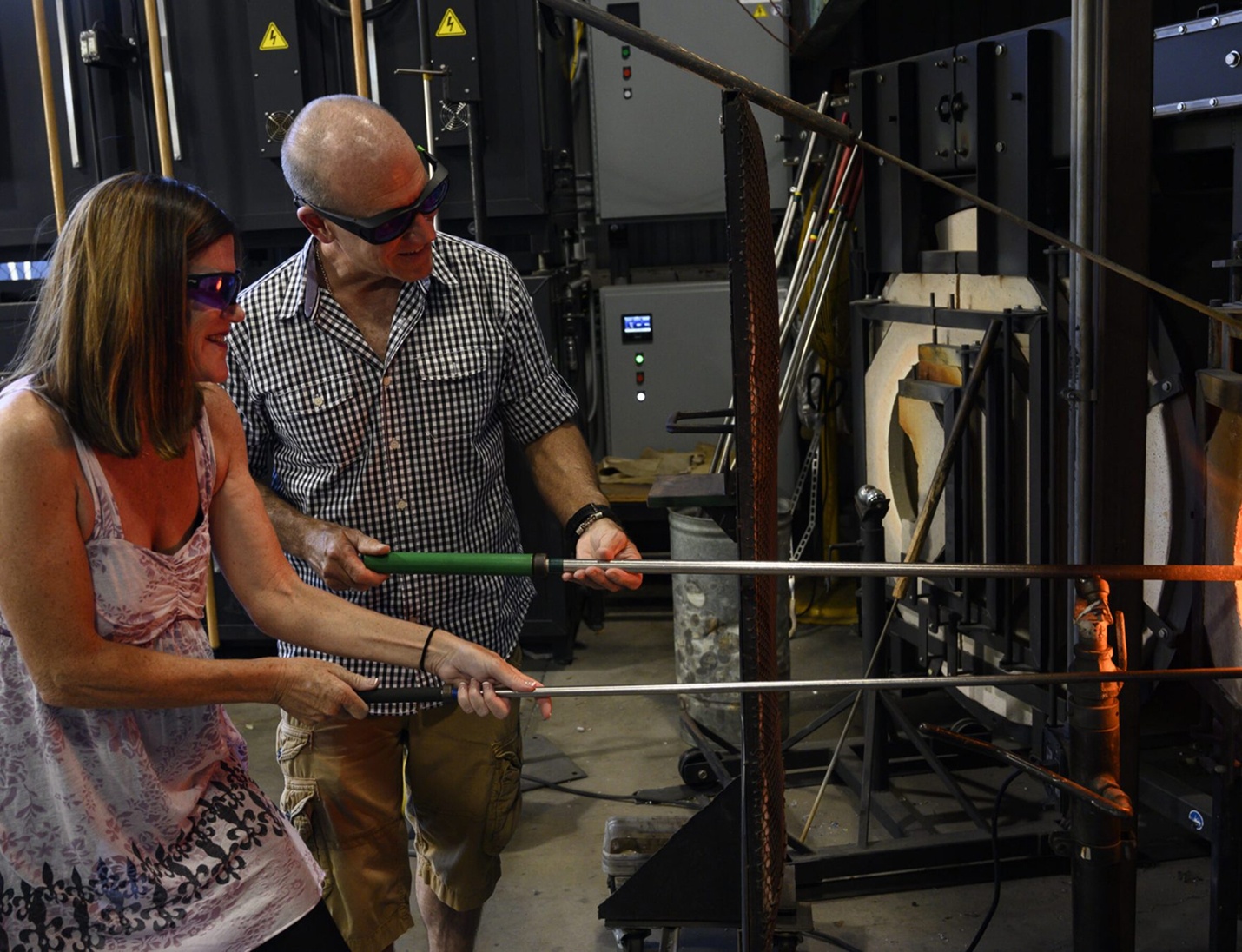 Visitors participating in a glassblowing activity at Morean Glass Studio & Hotshop with protective eyewear and furnaces