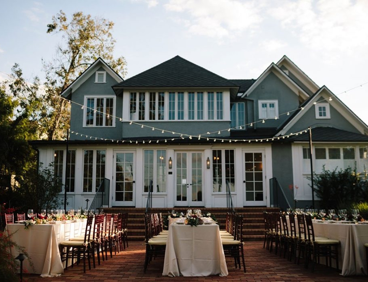 Outdoor wedding reception setup at The Capen House with string lights, long tables, and elegant place settings at sunset