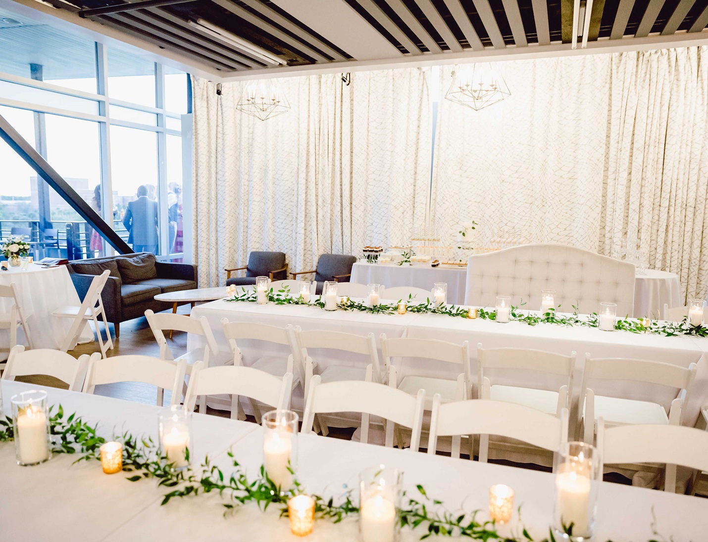 Modern indoor wedding reception at Rooftop 220 with white tables, candles, greenery decor, and natural light