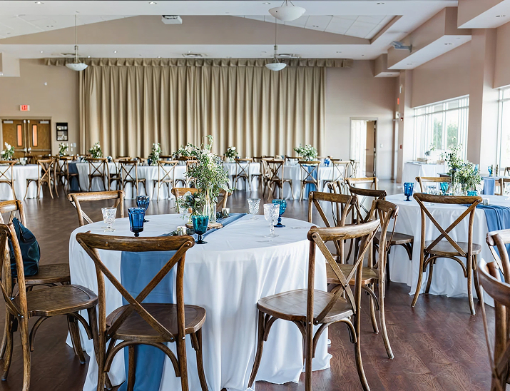 Indoor wedding reception at St. Pete Beach Community Center with wooden chairs, white linens, and blue glass accents