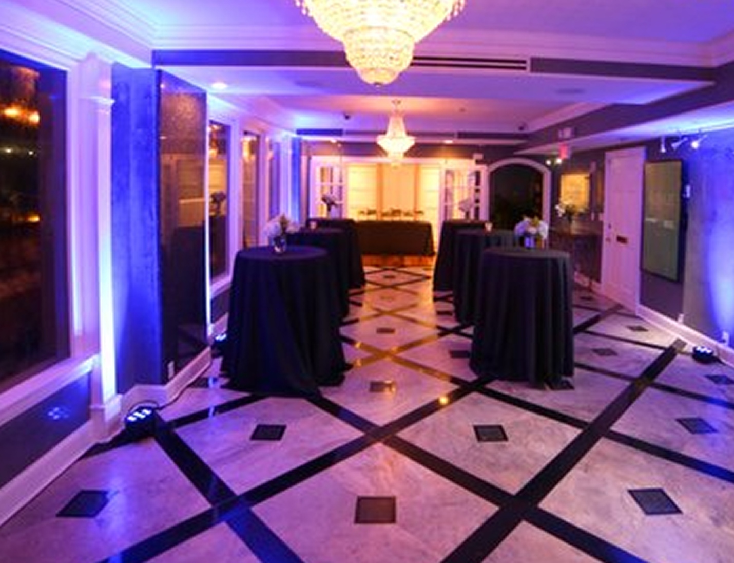 Elegant indoor cocktail space at Penthouse 450 with marble floors, chandeliers, black linens, and blue accent lighting