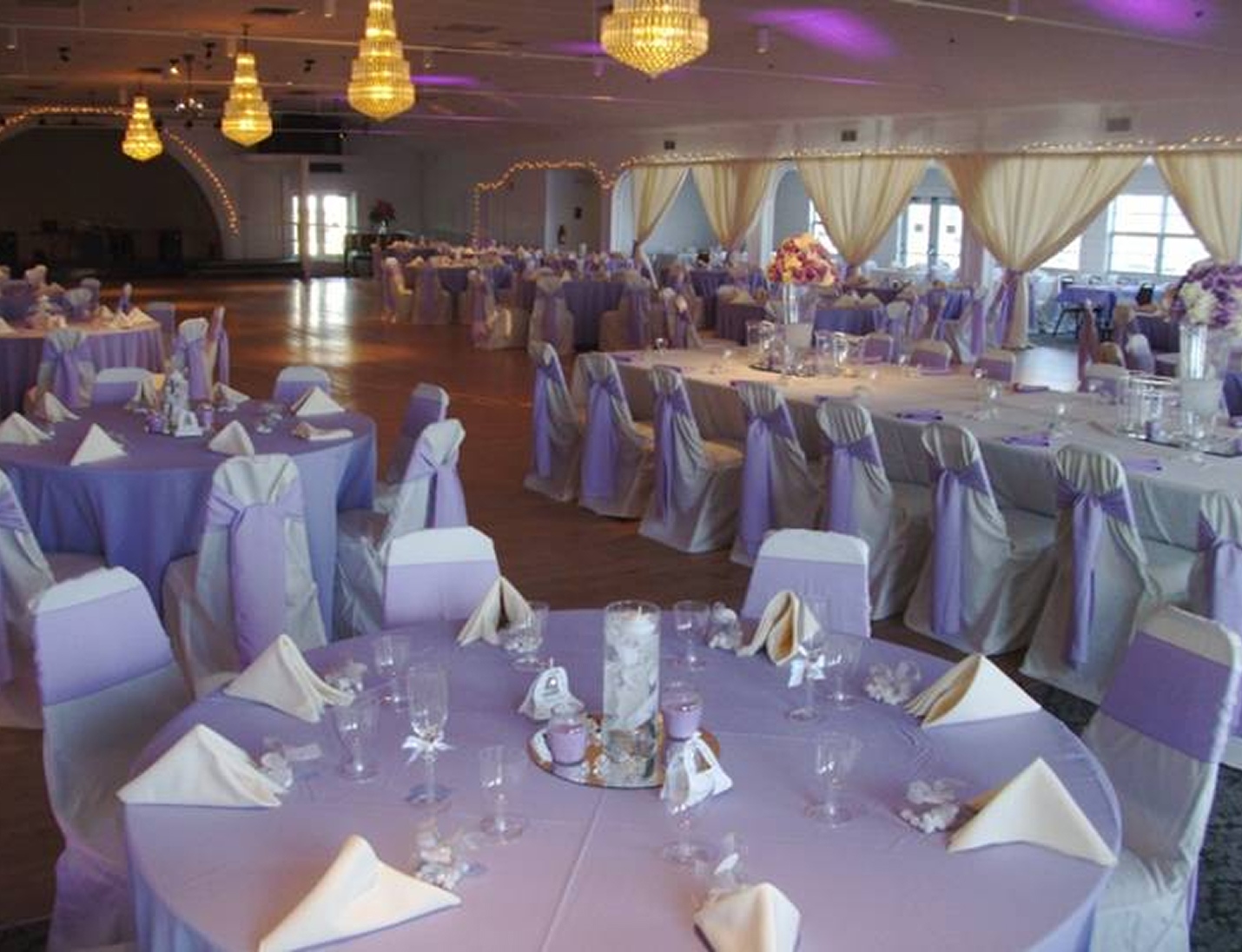 Elegant reception at Gulfport Casino Ballroom with chandeliers, lilac decor, draped curtains, and soft uplighting