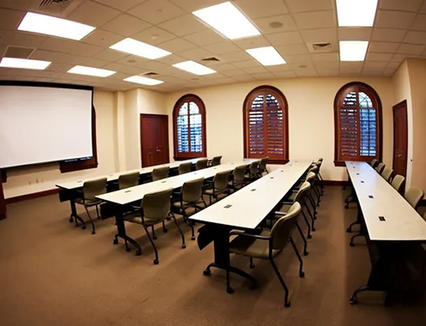 Conference room at Chester H Ferguson Law Center with long tables, chairs, a projector screen, and arched wooden windows