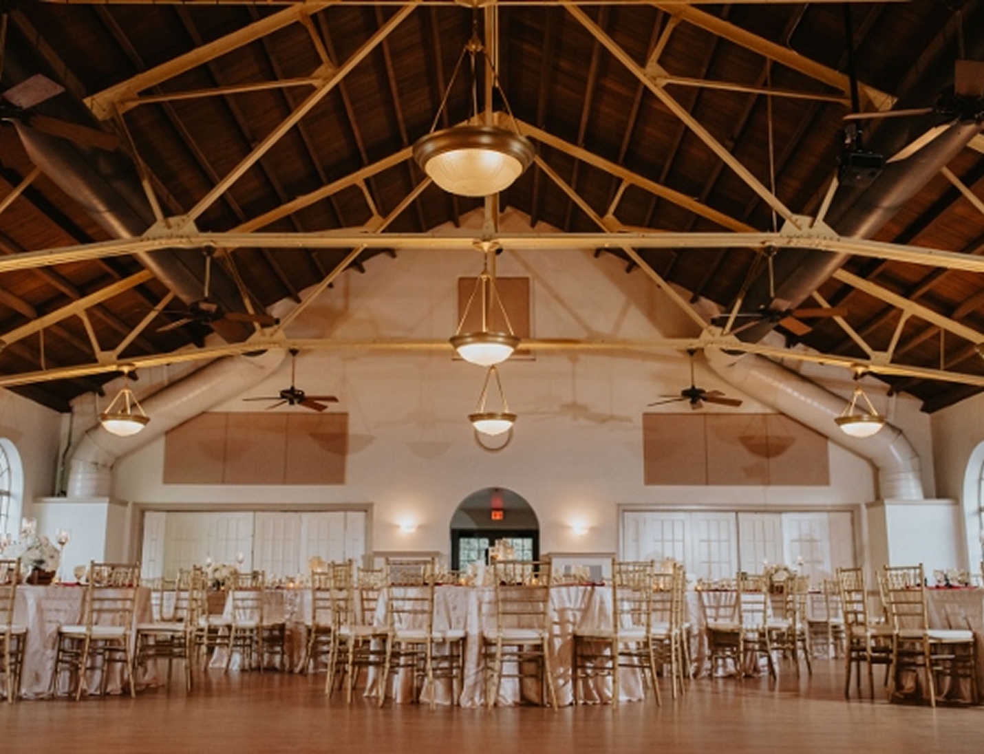 Elegant indoor wedding reception at Hollis Garden featuring gold chairs, round tables, and warm ambient lighting