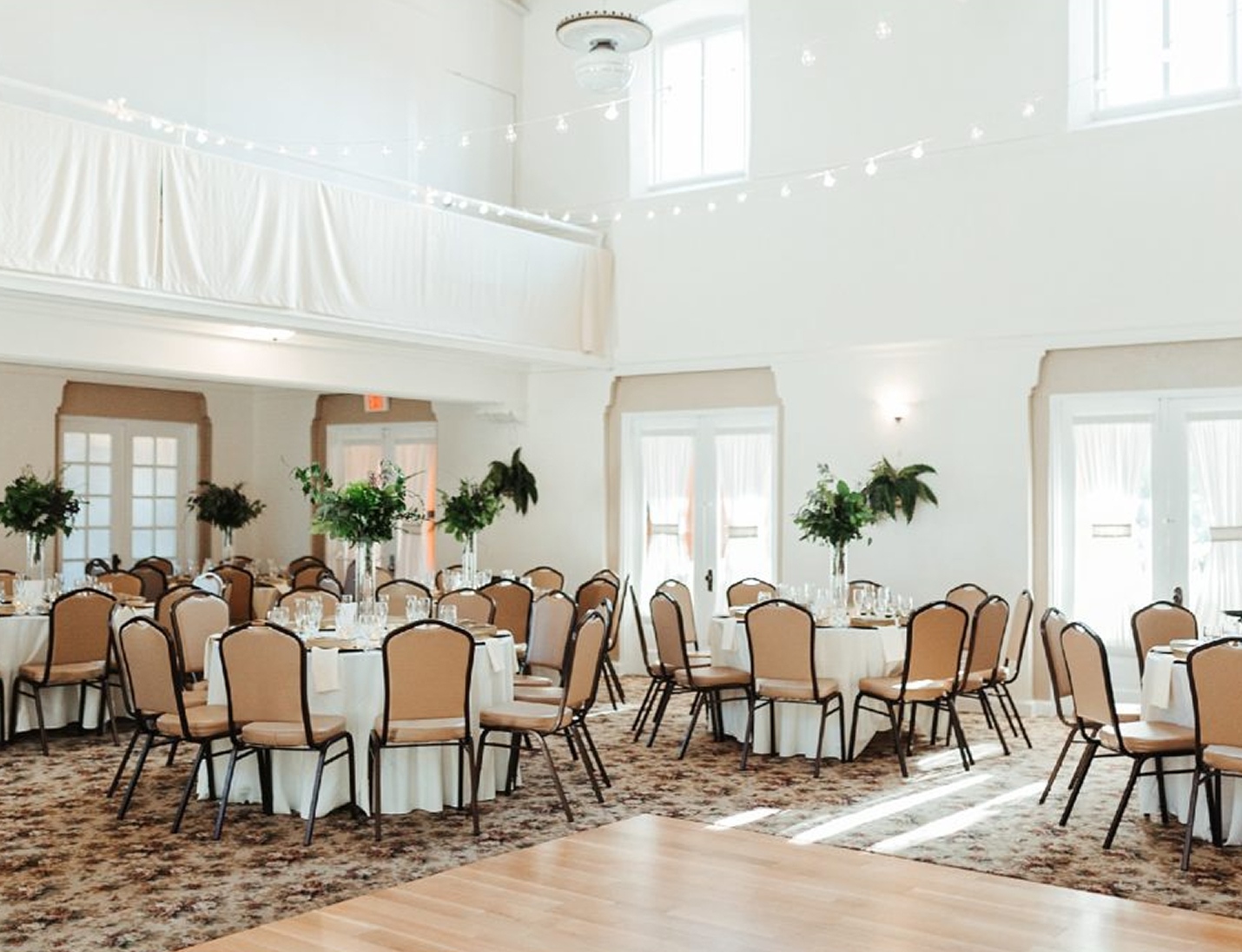Elegant indoor reception at St. Petersburg Women’s Club featuring round tables, tan chairs, greenery, and soft lighting