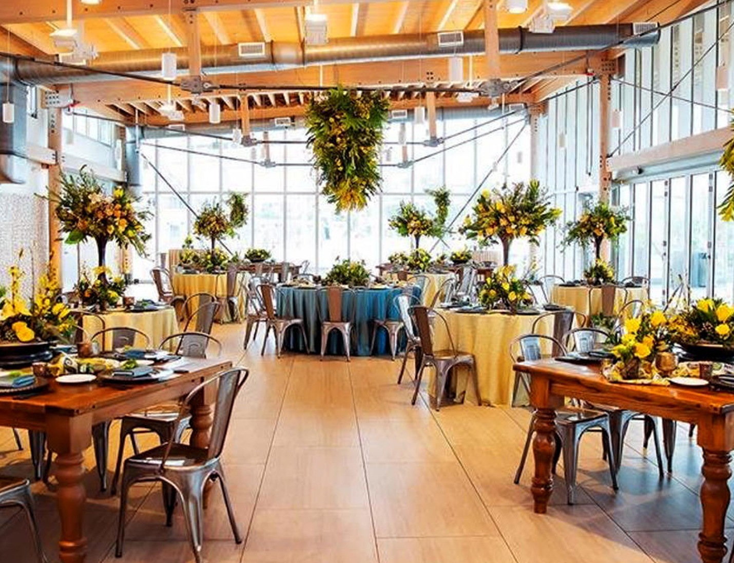 Indoor reception setup at Julian B Lane Park with wooden tables, yellow floral centerpieces, and large hanging greenery