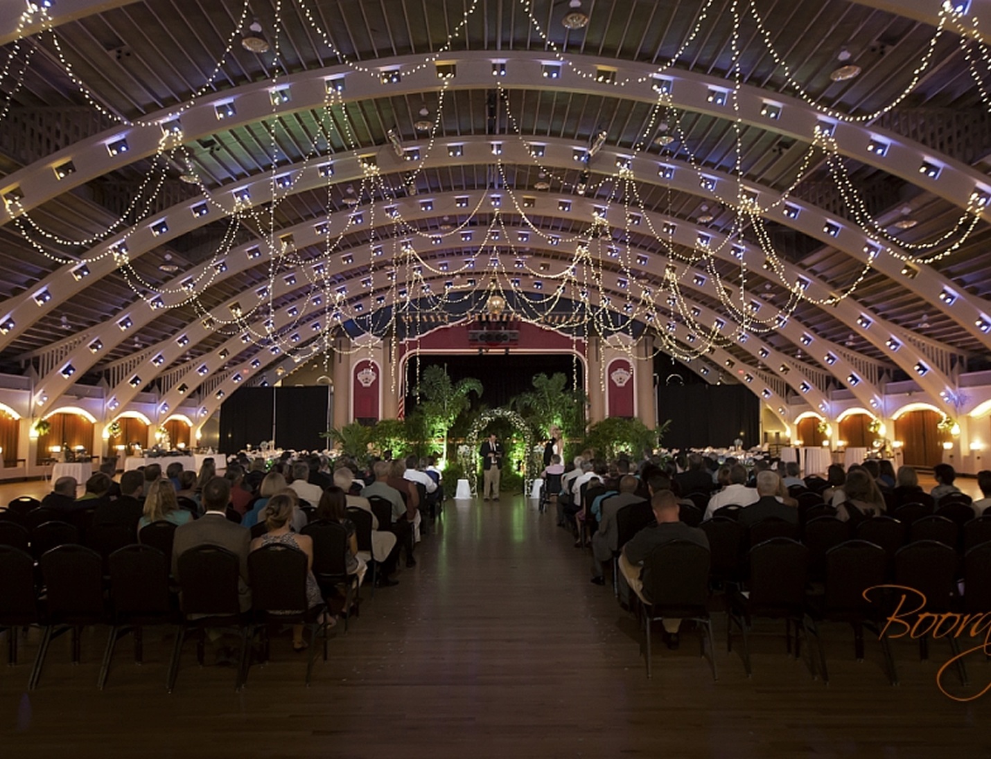 Ceremony at The Coliseum - St. Petersburg with an arched ceiling, string lights, and seated guests facing the stage