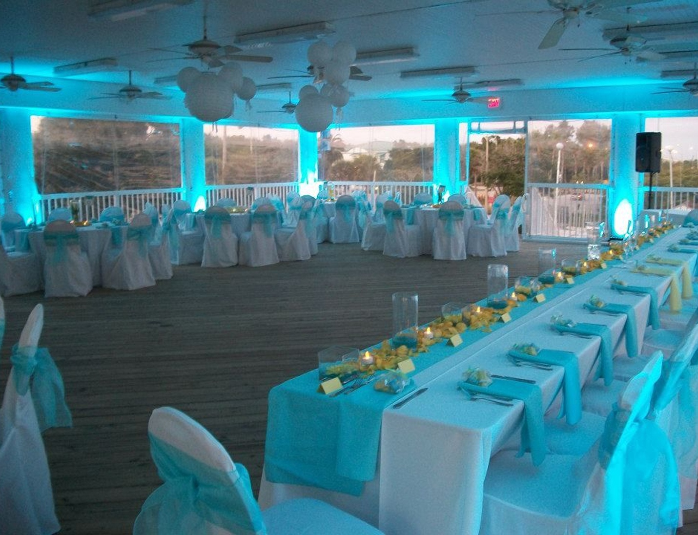 Indoor reception at Clearwater Community Sailing Center with blue uplighting, white chairs, and ocean view windows