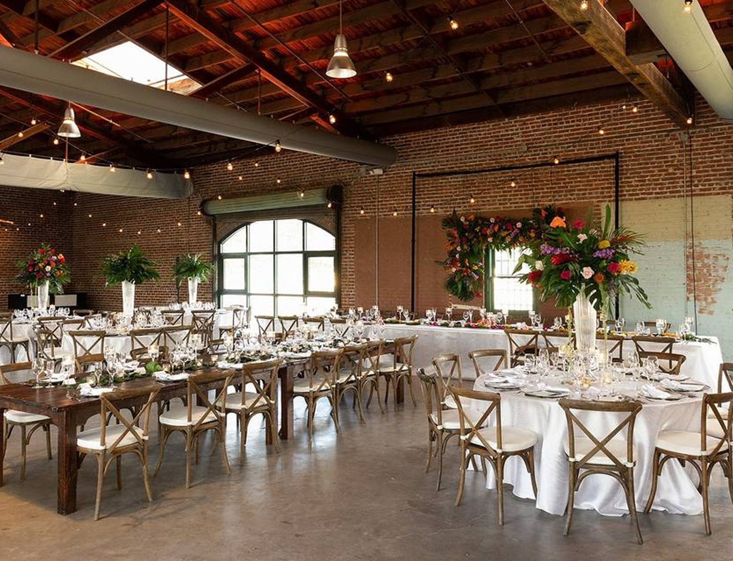 Industrial-style wedding setup at Morean Center for Clay with exposed brick walls, wooden beams, and floral centerpieces