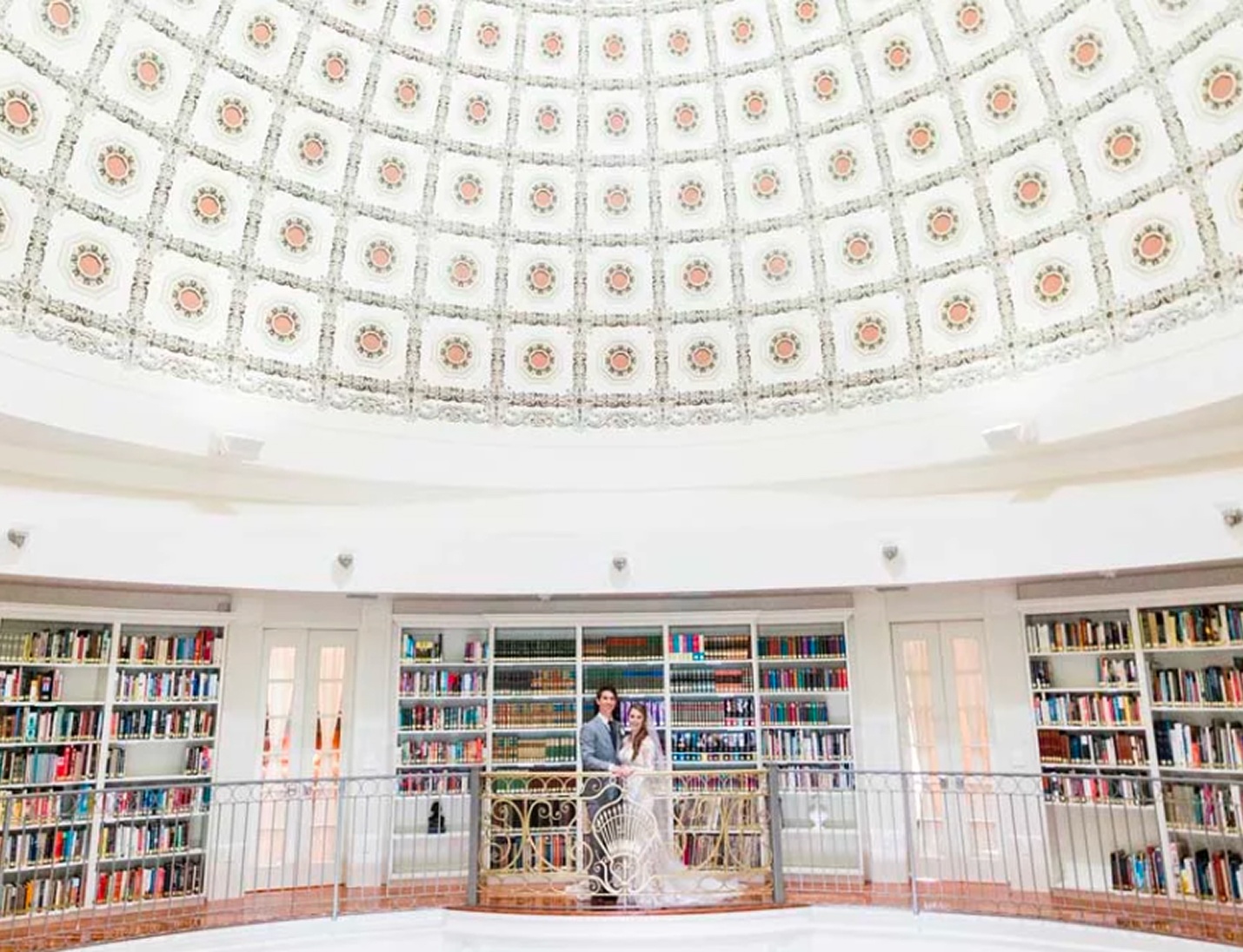 Bride and groom pose beneath the ornate domed ceiling at Whitehurst Gallery, framed by shelves of classic books