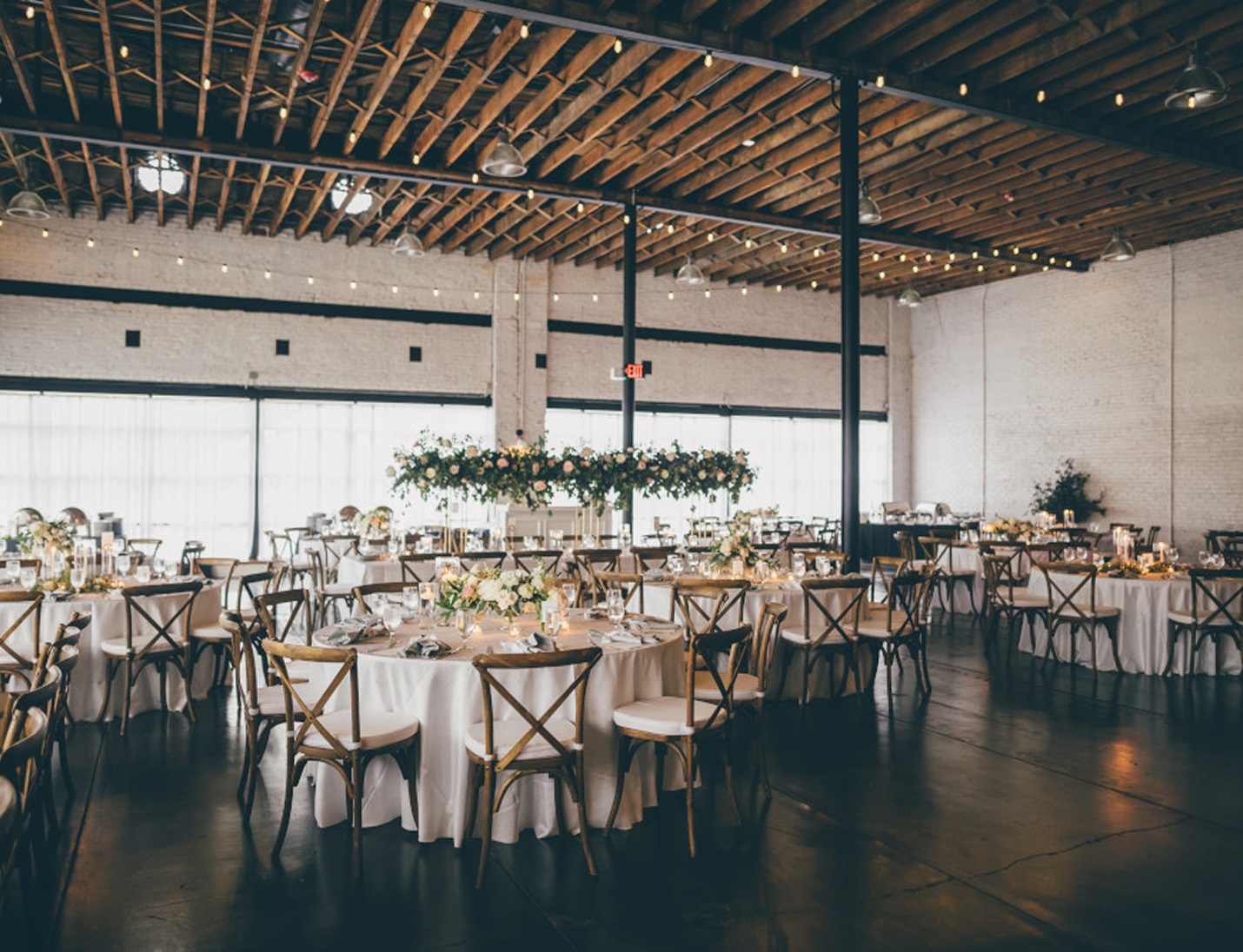 Modern industrial wedding reception at Haus 820 featuring wooden ceiling beams, string lights, and elegant round tables