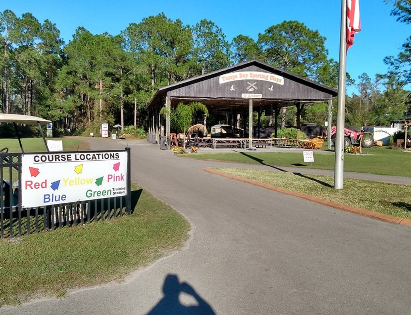 Outdoor entrance at Tampa Bay Sporting Clays with wooden pavilion, course sign, and surrounding trees