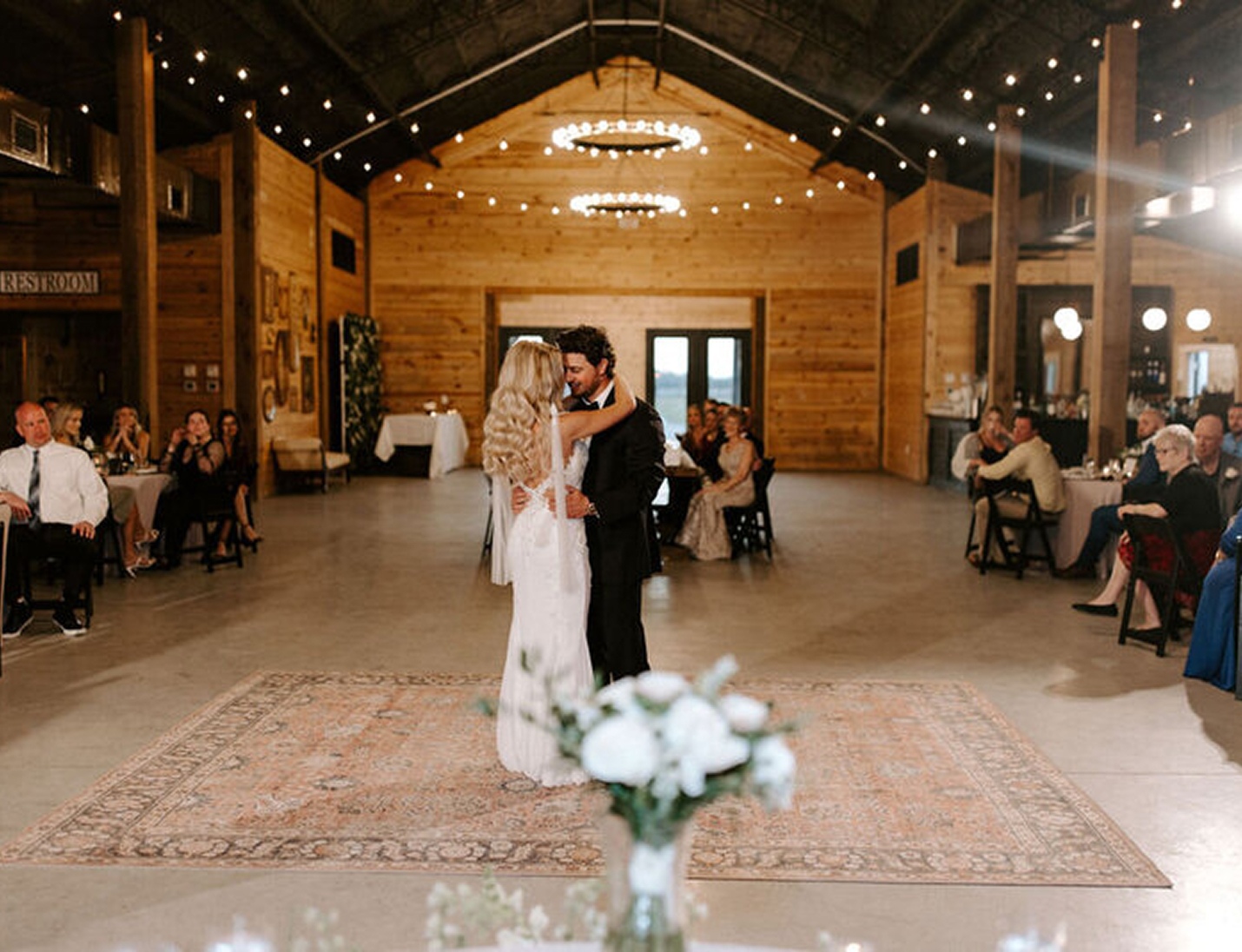 A couple dancing at Lovelock Ranch reception hall with string lights, and guests seated around the dance floor