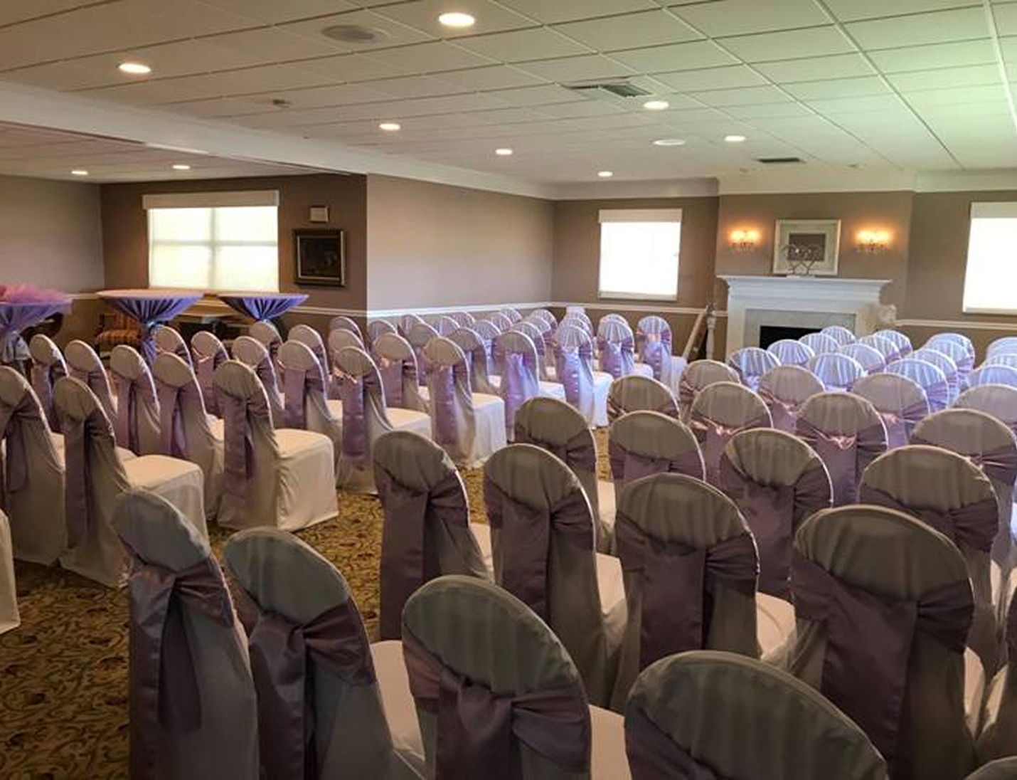 Indoor ceremony at GFWC Tampa Women’s Club with rows of white chairs tied with lavender bows and warm lighting
