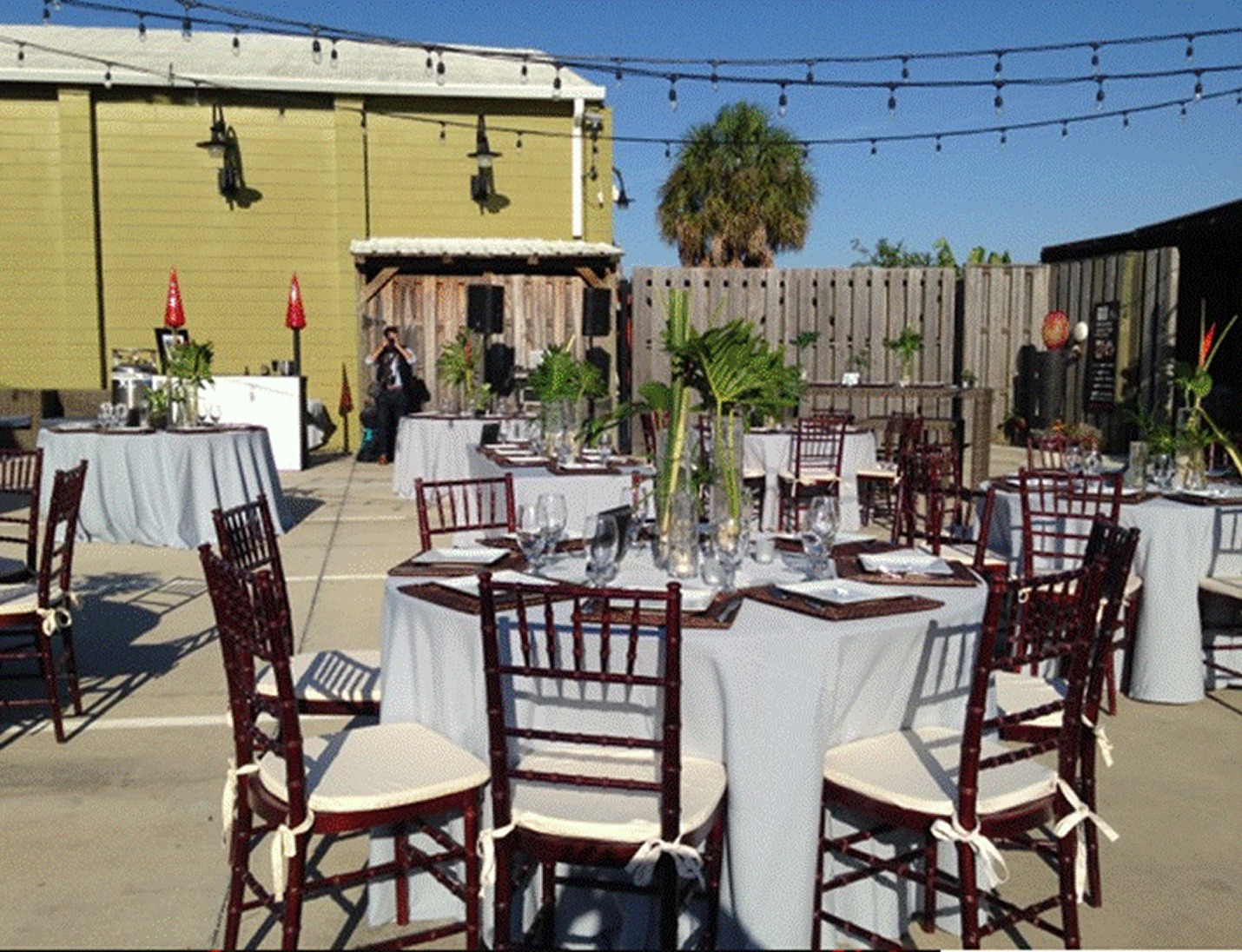 Outdoor reception at Duncan McClellan Gallery with round tables, wood chairs, palm decor, and hanging string lights