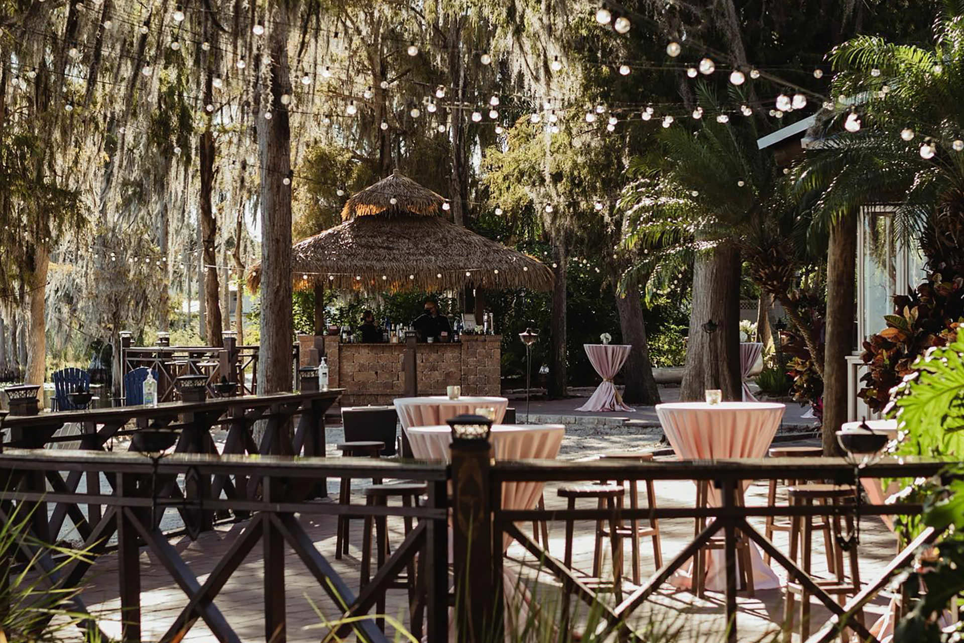 Outdoor tiki-style setup at Paradise Cove Orlando with cocktail tables, palm trees, and glowing string lights