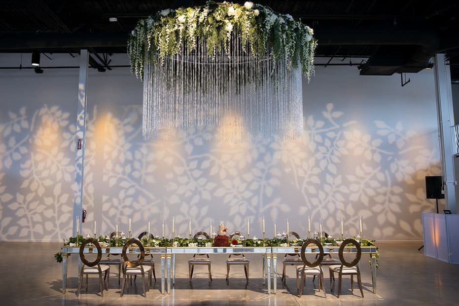 Modern setup at Canvas Event Venue with a long floral table, a cascading chandelier, and artistic wall lighting