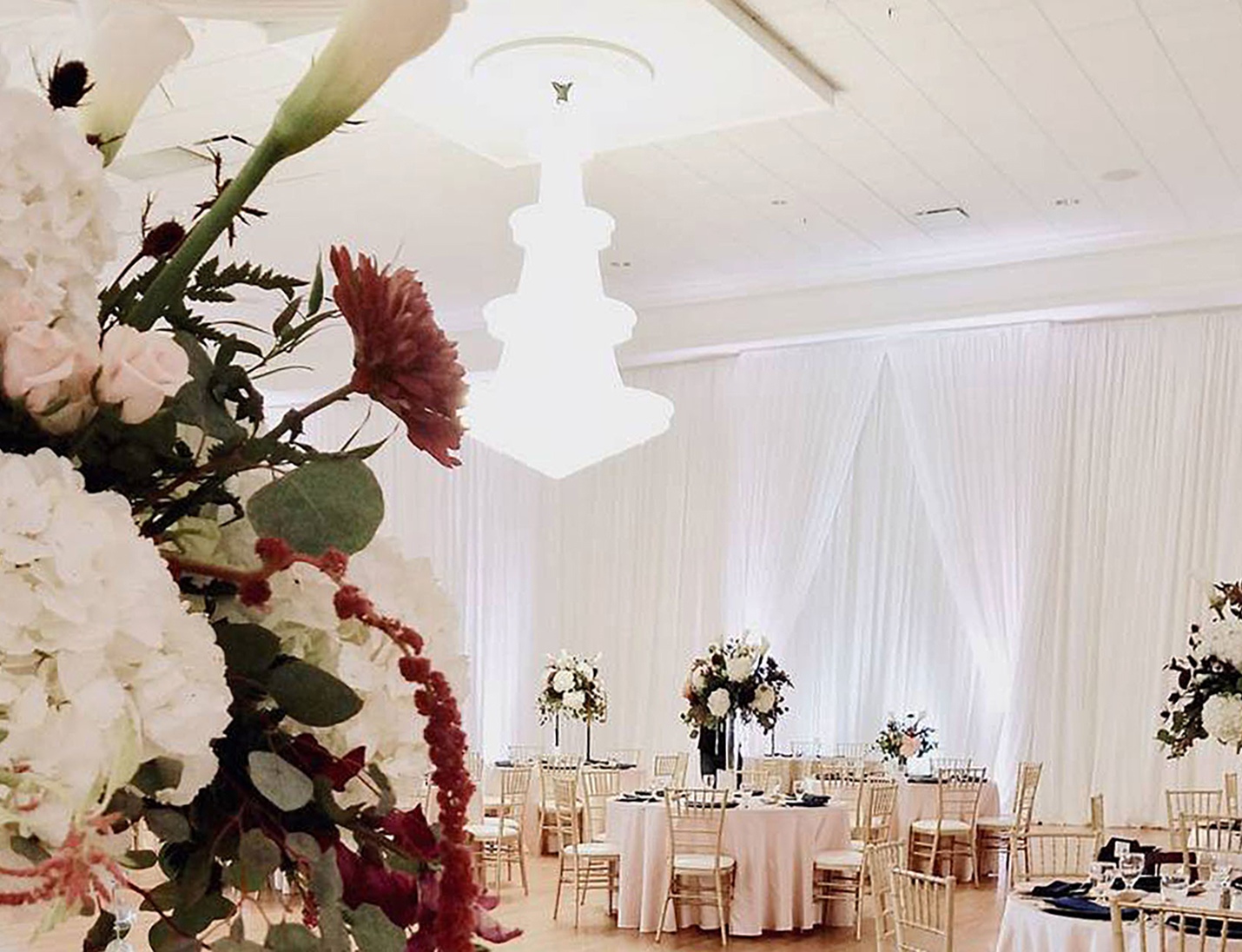 Elegant ballroom at The Regent with tall floral centerpieces, gold chairs, soft draped walls, and warm ambient lighting