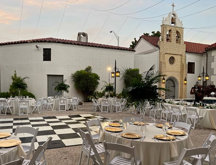Outdoor courtyard setup at The Bishop Museum of Science and Nature with round tables, gold plates, and string lights.