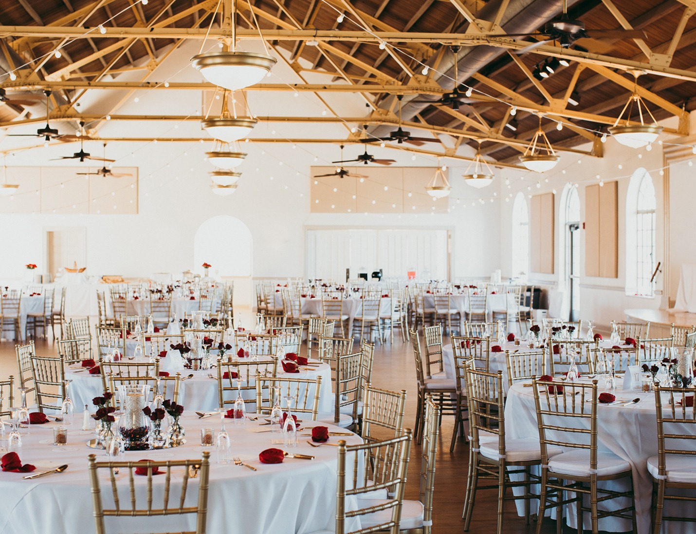 Elegant reception setup at Magnolia Building with round tables, gold chairs, wooden beams, and string lights
