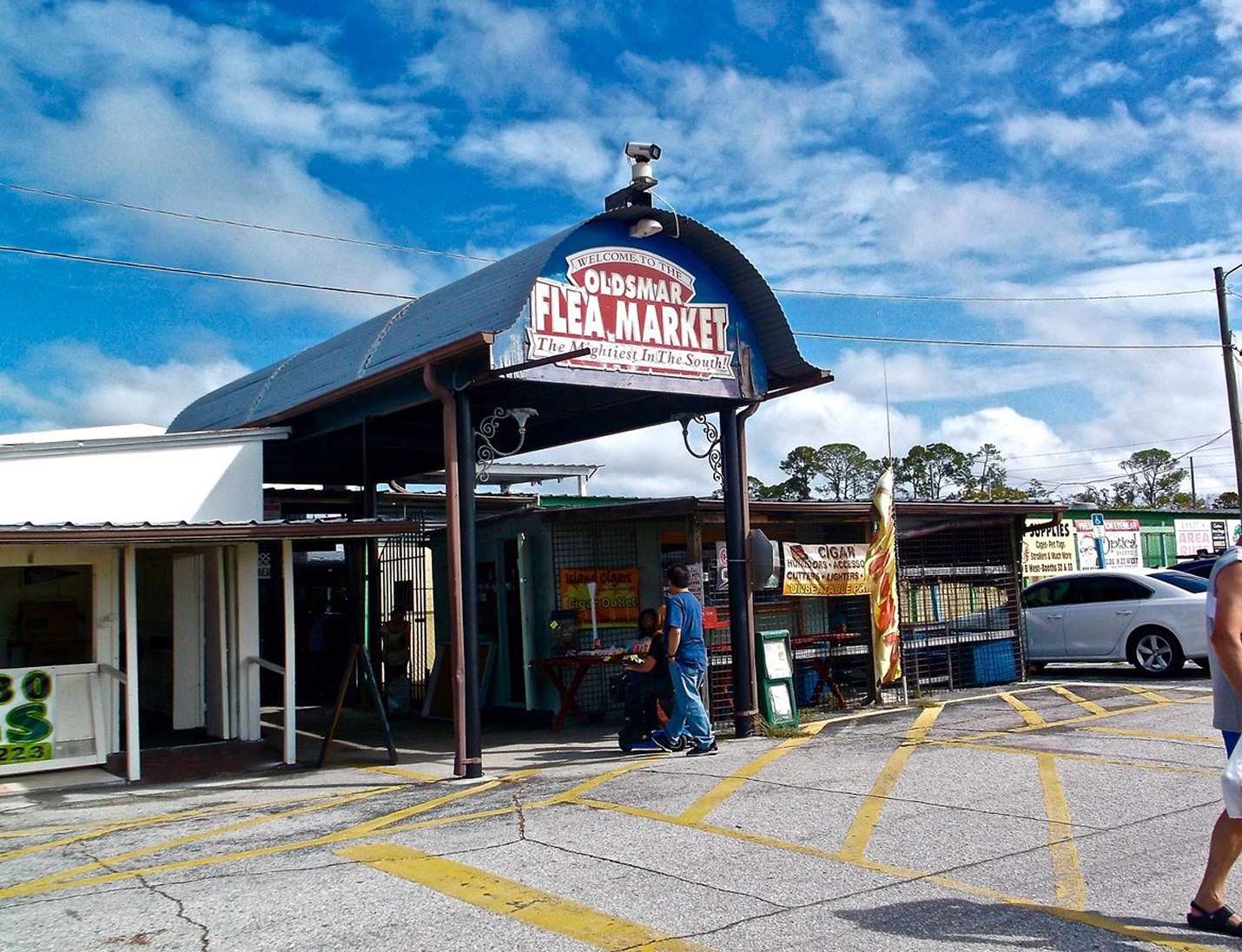 Outdoor entrance of The Venue at Oldsmar Flea Market with a metal archway, parking area, and bright blue sky