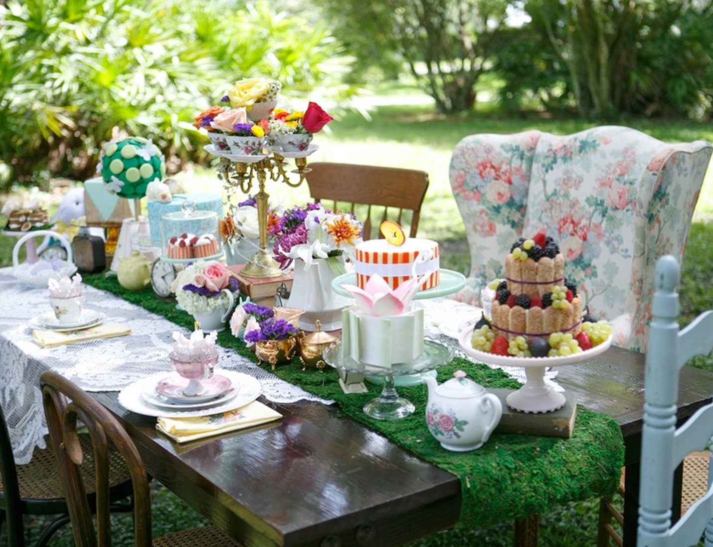 Colorful outdoor tea party setup at USF Botanical Gardens with floral décor, vintage tableware, and layered dessert