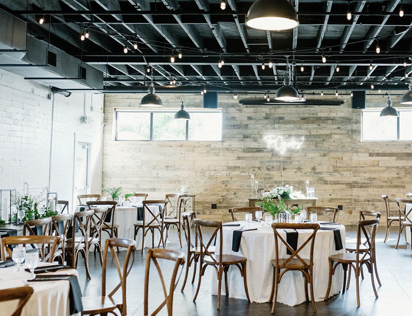Modern industrial-style setup at The West Events with wooden walls, string lights, and round tables with simple decor
