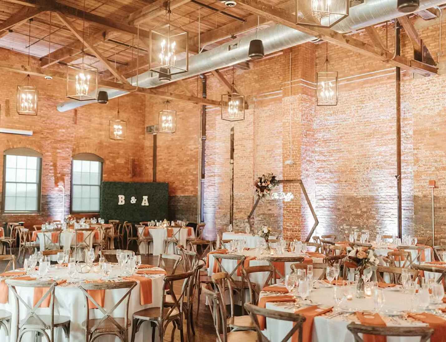 Rustic event setup at Armature Works with brick walls, wooden beams, hanging lights, and decorated round tables.