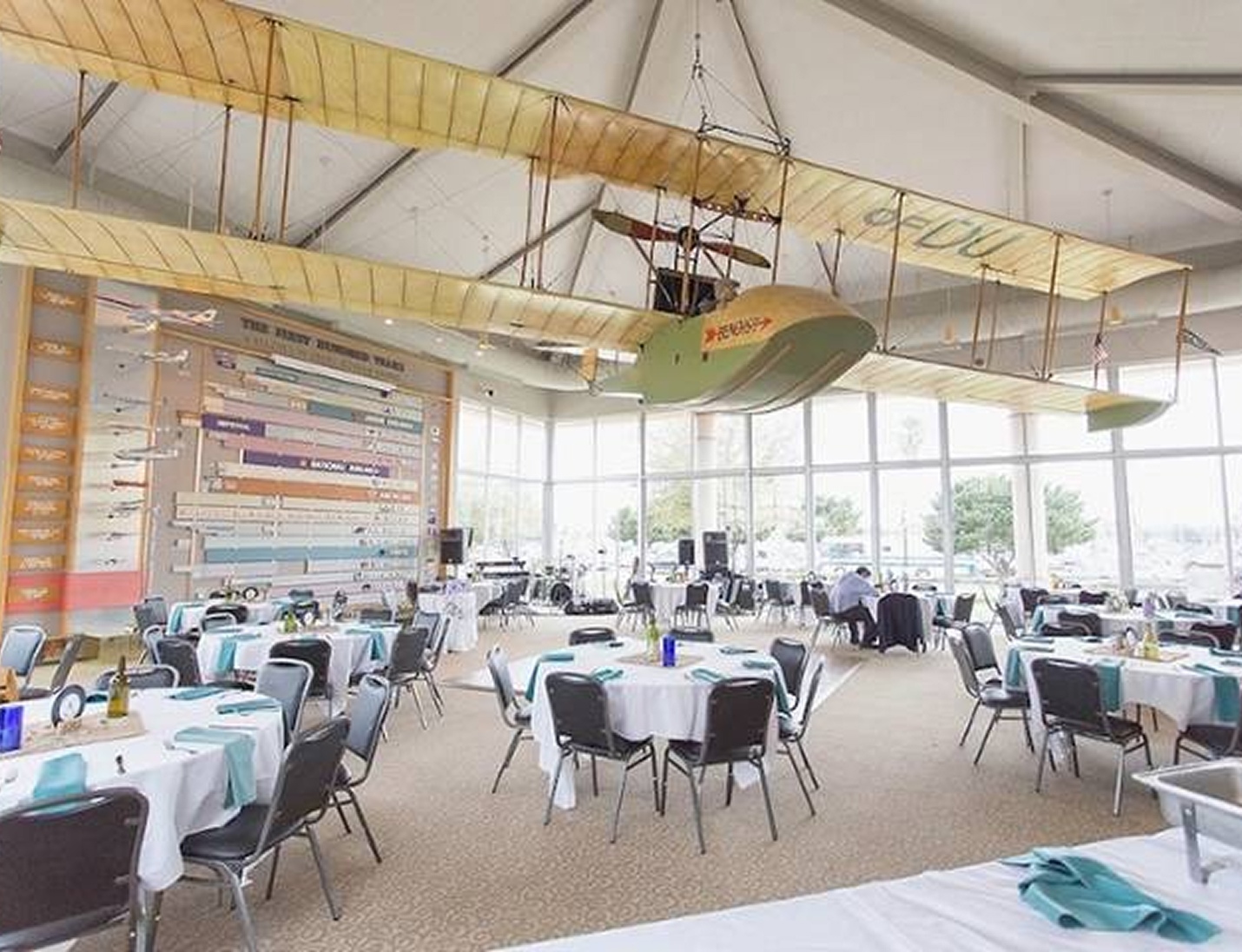 Event setup at St. Petersburg Museum of History featuring vintage aircraft, large windows, and decorated round tables