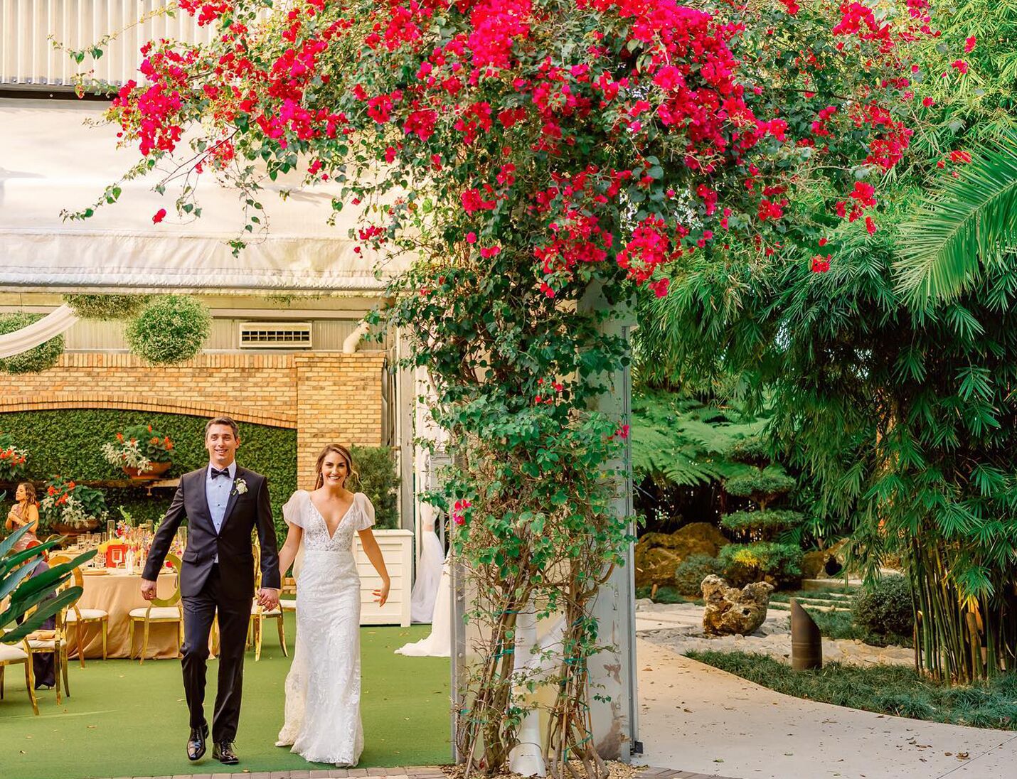 Bride and groom walking through a floral arch at Hardeman’s Secret Garden, surrounded by greenery and elegant decor