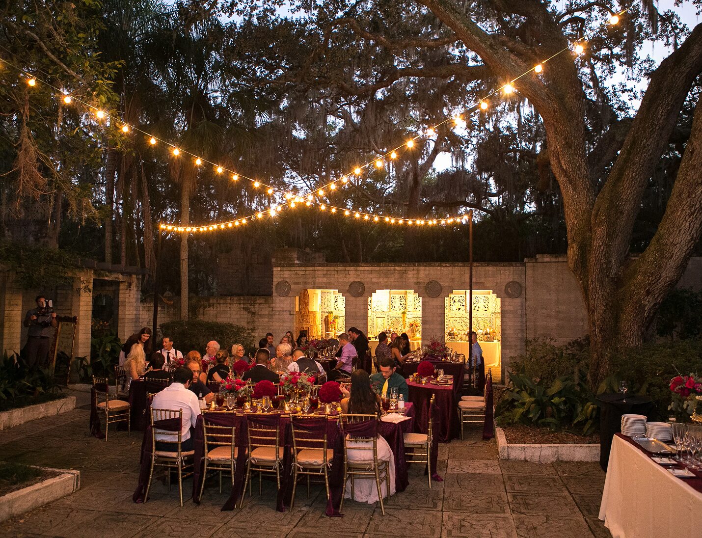 Evening event at Art & History Museums - Maitland with string lights, dining tables, and guests under large oak trees