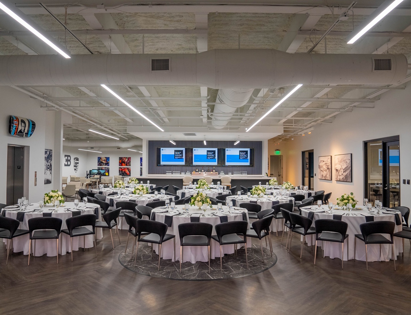 Modern event setup at The Motor Enclave with black chairs, round tables, floral centerpieces, and large digital screens