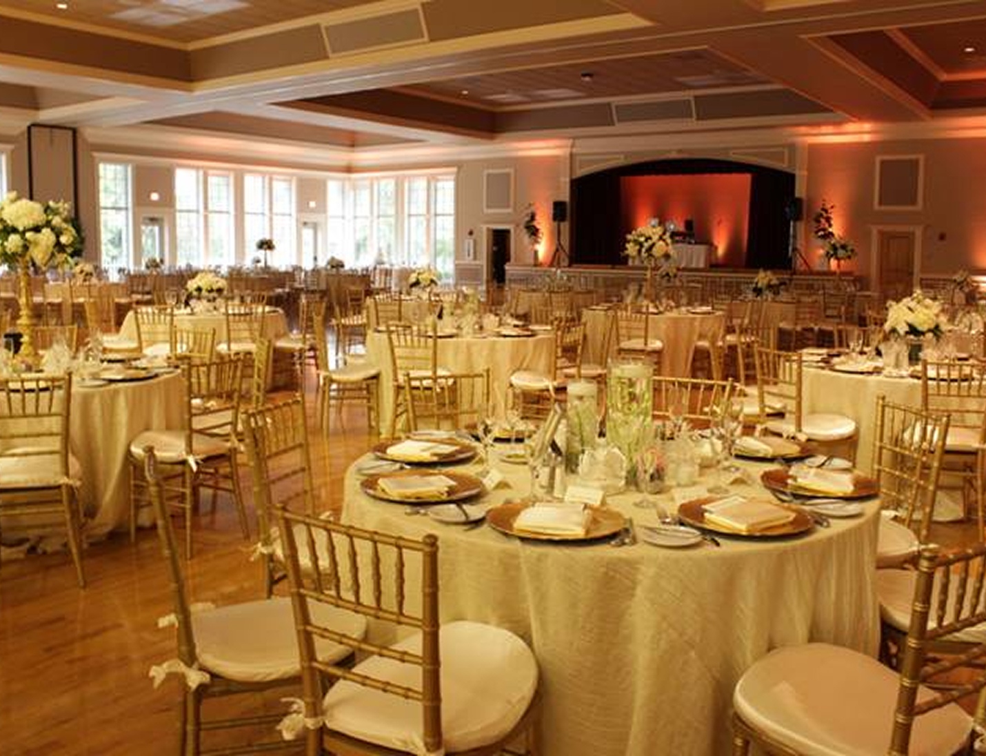 Elegant ballroom setup at Higgins Hall with round tables, gold chairs, floral centerpieces, and soft amber lighting