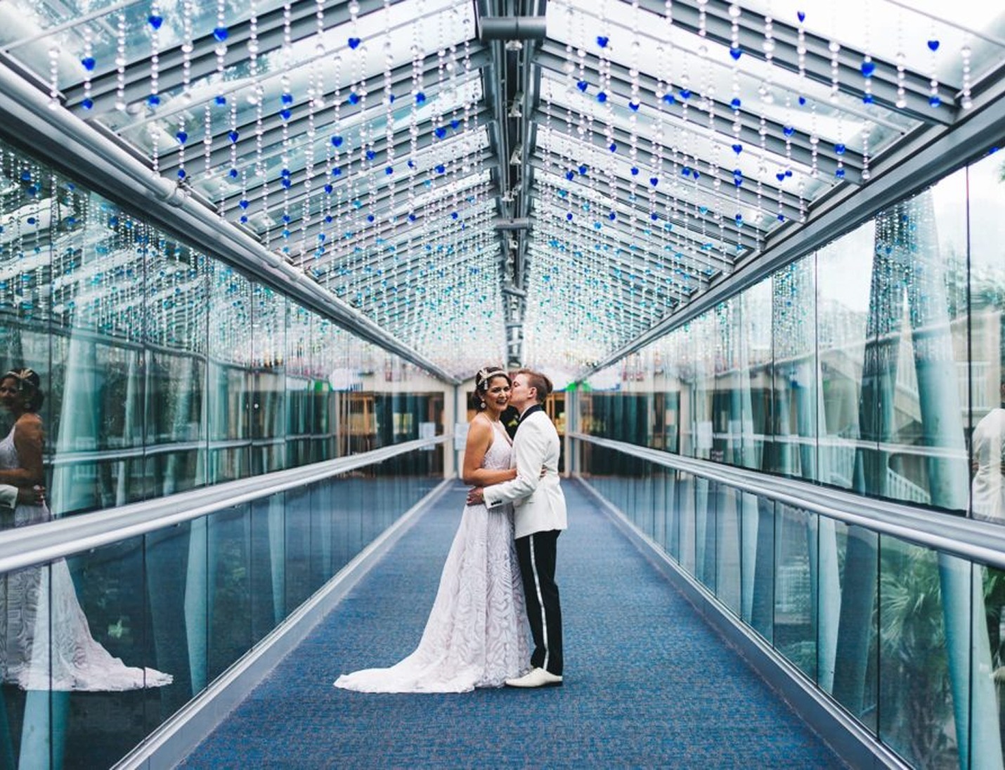 Bride and groom embracing in a glass walkway at Orlando Science Center with hanging blue lights and mirrored reflections