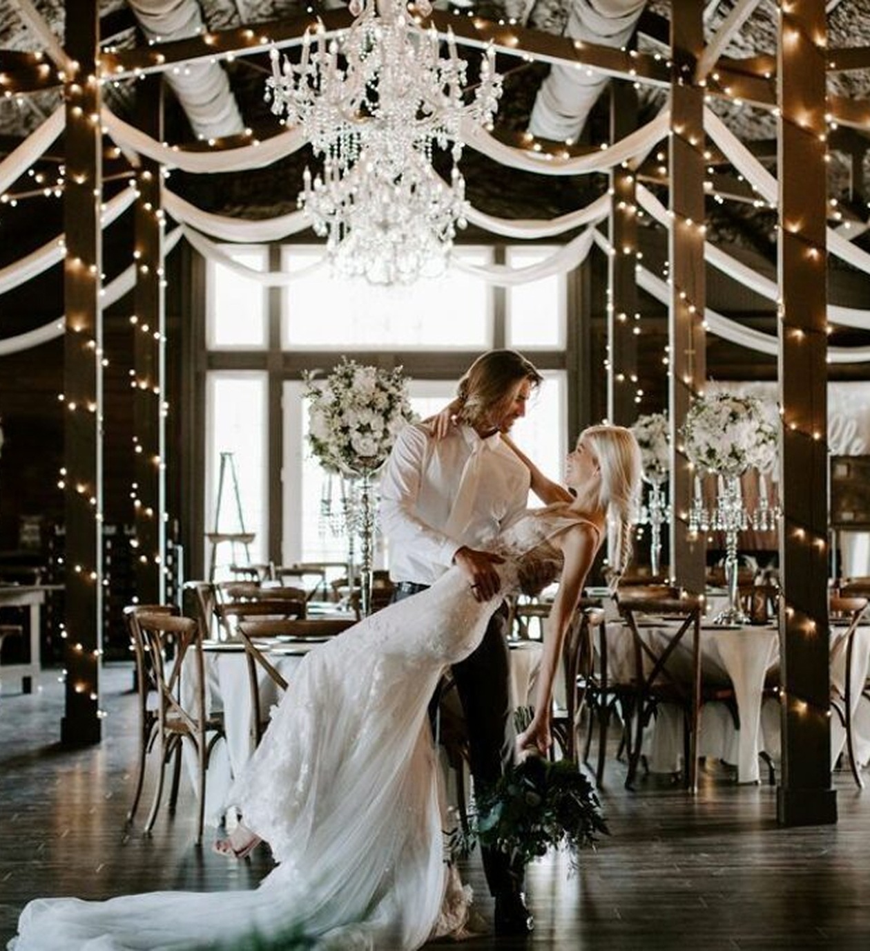 Bride and groom sharing a romantic dance under chandeliers and string lights at Ever After Farms barn venue