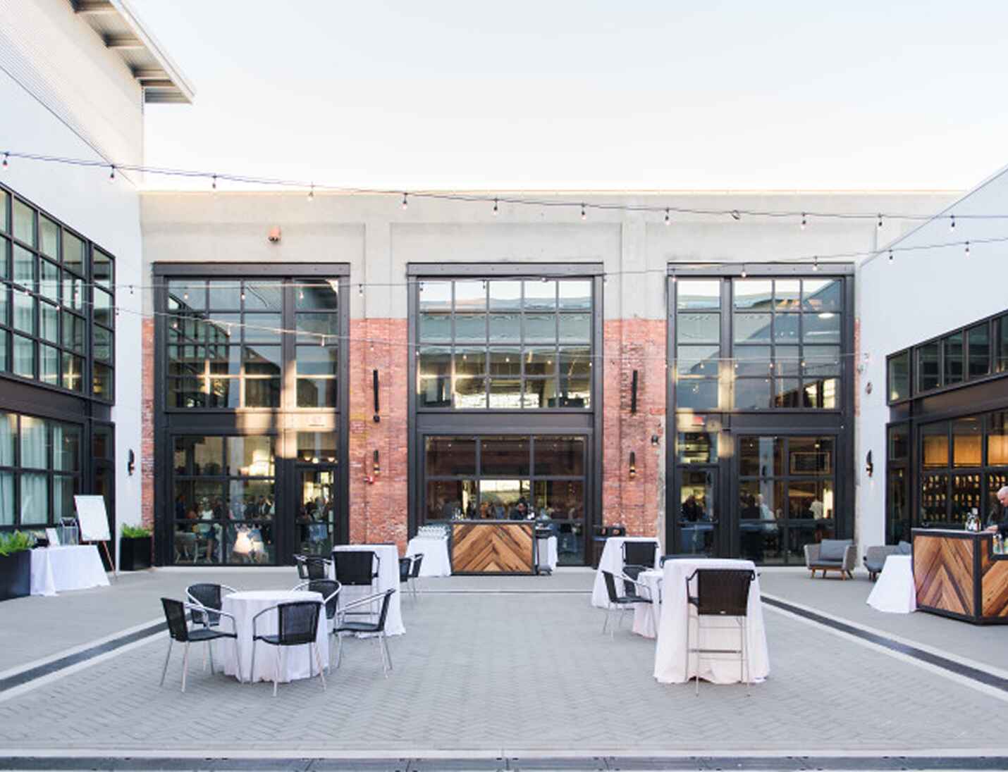 Armature Works courtyard setup with cocktail tables, string lights, and industrial brick and glass architecture