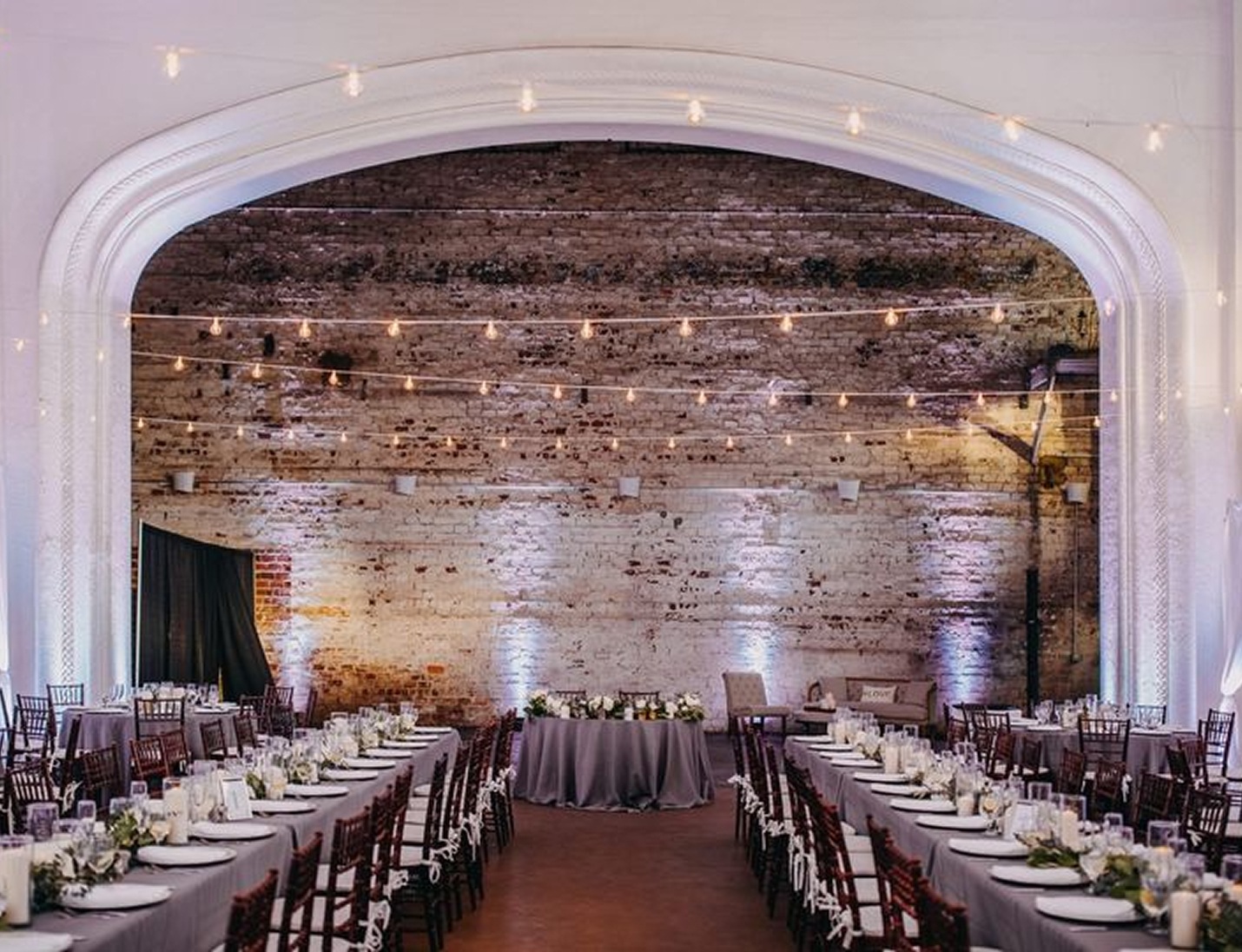 Rialto Theatre Tampa reception with long banquet tables, exposed brick backdrop, string lights and elegant neutral decor