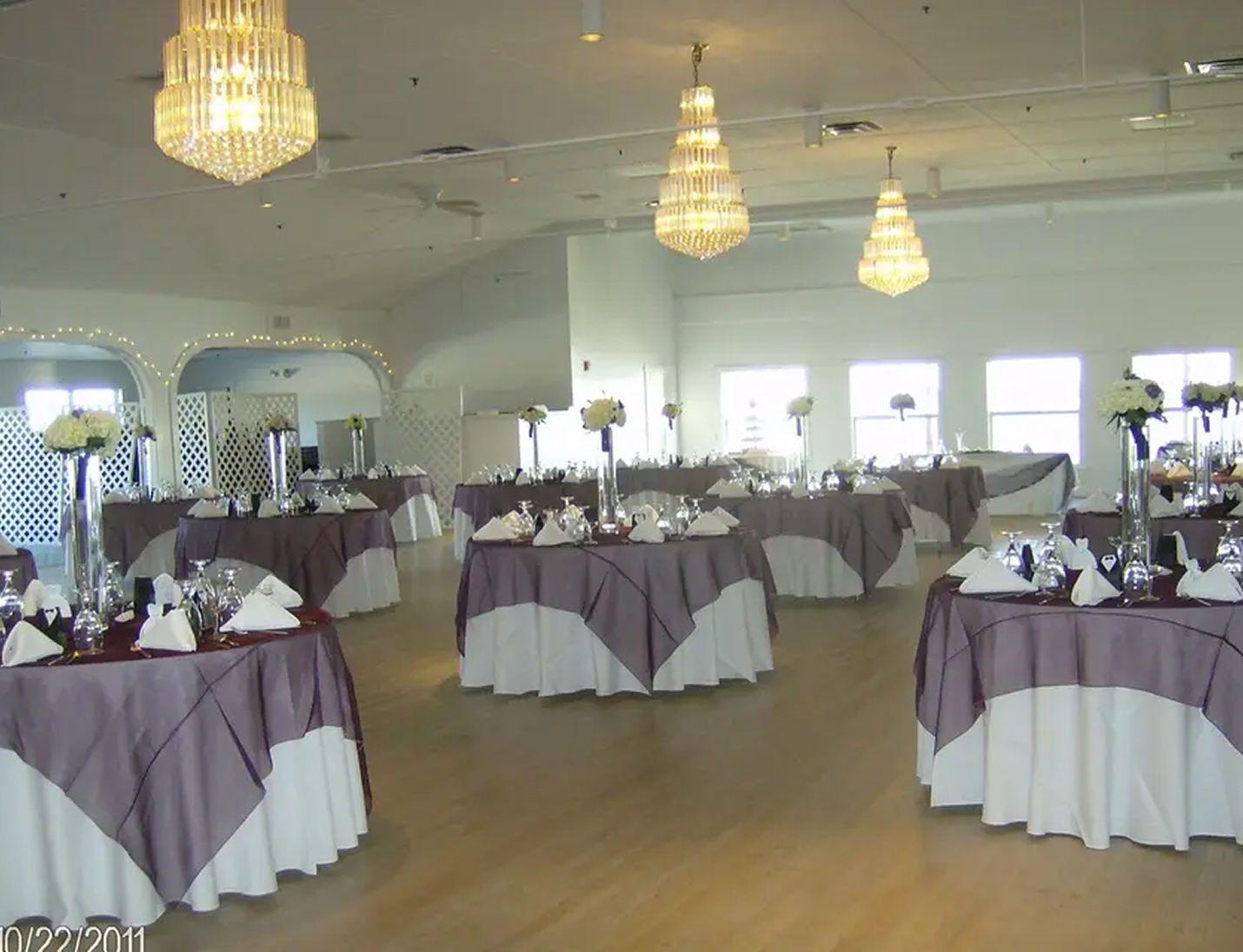 Gulfport Casino Ballroom setup with round tables, white and lavender linens, and chandeliers overhead