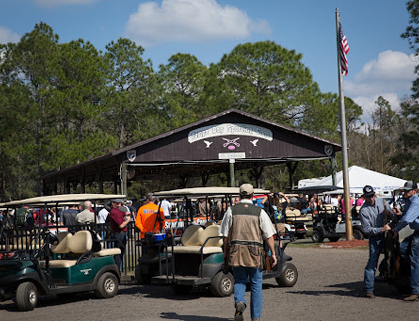 Tampa Bay Sporting Clays outdoor event area with guests, golf carts, and lodge entrance under pine trees
