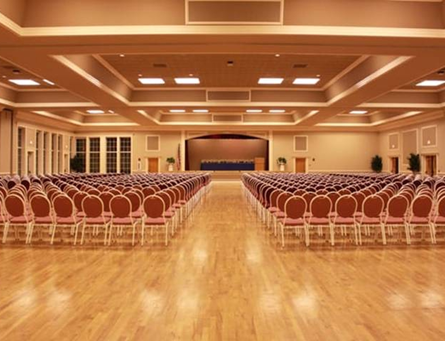 Large ballroom at Higgins Hall with rows of chairs facing a stage, wood flooring, high ceilings, and warm lighting